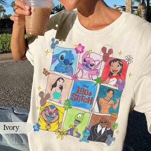 Puede incluir: Camiseta de color marfil con un gr&aacute;fico colorido de personajes de la pel&iacute;cula de Disney Lilo & Stitch. El dise&ntilde;o incluye im&aacute;genes de Stitch, Lilo y otros personajes en un patr&oacute;n de cuadr&iacute;cula. El texto "Lilo & Stitch" tambi&eacute;n es visible.