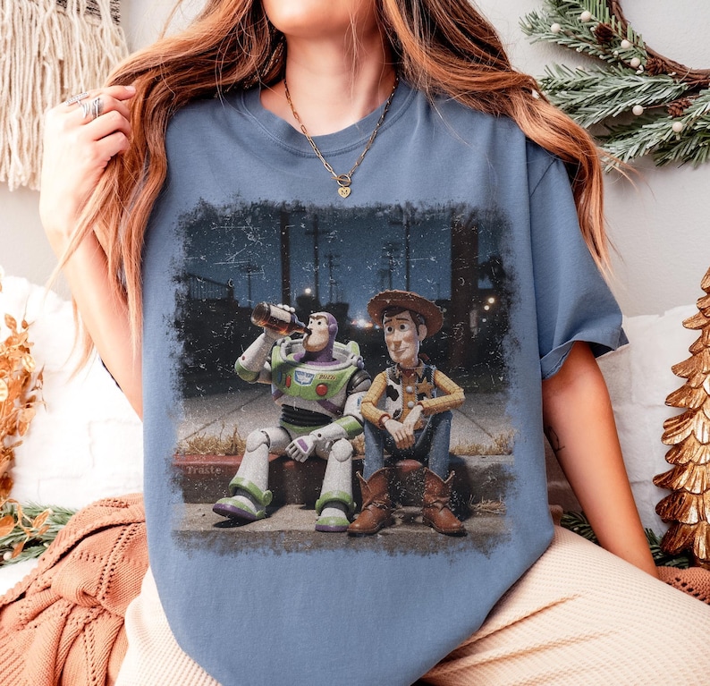 Puede incluir: Camiseta azul con un gr&aacute;fico de Buzz Lightyear y Woody de Toy Story. Buzz est&aacute; bebiendo de una botella, mientras que Woody est&aacute; sentado a su lado. El gr&aacute;fico tiene un aspecto envejecido y vintage.