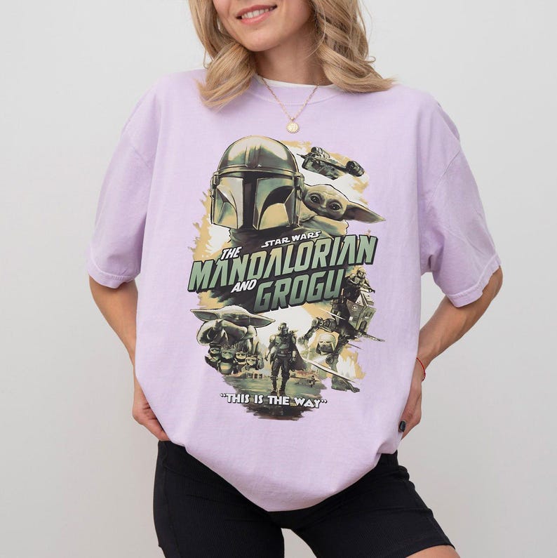 K&ouml;nnte beinhalten: Ein helllila T-Shirt mit einer Grafik aus der Star Wars-Serie "The Mandalorian and Grogu". Das Design zeigt Bilder von Mandalorian, Grogu und anderen Charakteren mit dem Satz "This is the Way."