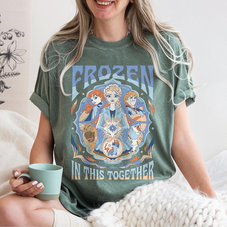 May include: Green t-shirt featuring the word "FROZEN" in blue and a graphic of characters from the movie. The phrase "IN THIS TOGETHER" is below the graphic. The shirt is a relaxed fit.