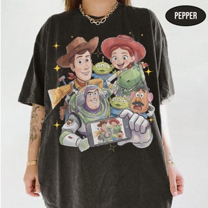 May include: Black t-shirt featuring a graphic of characters from the animated movie Toy Story. The design includes Woody, Buzz Lightyear, Jessie, and other characters. The word "PEPPER" is printed on the top right corner.