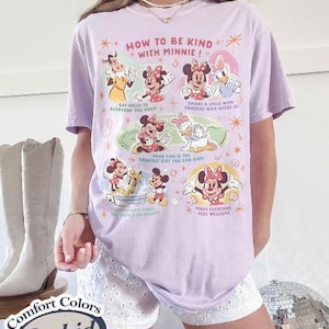 Peut inclure: T-shirt Comfort Colors lilas avec un motif de Minnie Mouse et l'inscription "HOW TO BE KIND WITH MINNIE!". Le t-shirt pr&eacute;sente d'autres phrases et est port&eacute; avec un short blanc. L'image comprend des bottes blanches.