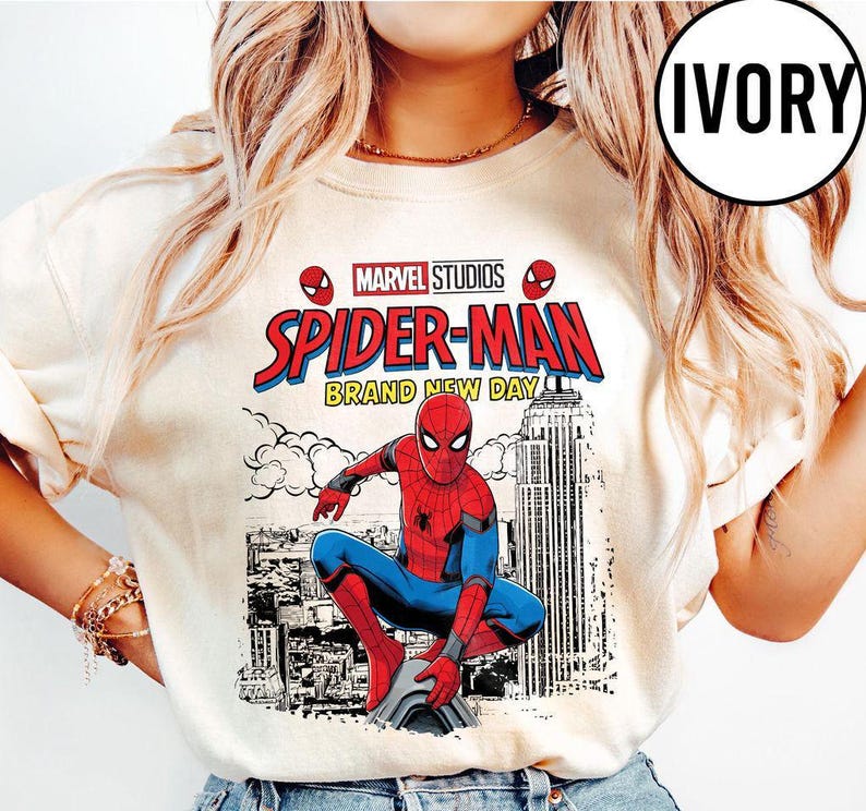 Pode incluir: Camisola de cor marfim com um design de banda desenhada do Homem-Aranha. O gr&aacute;fico inclui o log&oacute;tipo da Marvel Studios, as palavras "Spider-Man Brand New Day" e uma ilustra&ccedil;&atilde;o do Homem-Aranha. A camisola tem gola redonda.