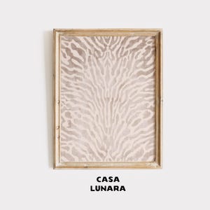 May include: A rectangular wall art piece in a light wood frame featuring a vertical, symmetrical abstract pattern in shades of beige and cream. The design consists of organic, branching lines that radiate from the center. The text CASA LUNARA is below.