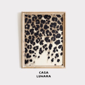 May include: A rectangular wall art print featuring a black and beige leopard print pattern, encased in a light-toned wooden frame. Below the framed artwork, the text CASA LUNARA is printed in a bold, black, sans-serif font on a plain background.