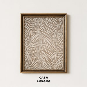 Puede incluir: Una pieza de arte mural rectangular en un marco de tono bronce oscuro que presenta un estampado vertical con un patrón repetitivo de rayas beige y blancas. El texto CASA LUNARA está impreso en letras mayúsculas negras en la parte inferior.