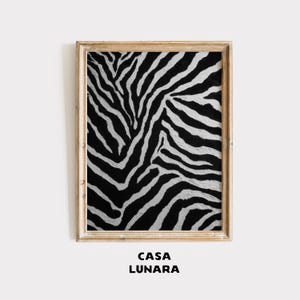 May include: A rectangular wall art print featuring a high-contrast black and white zebra stripe pattern, encased in a light-toned wooden frame. Below the framed artwork, the text CASA LUNARA is printed in a bold, black, sans-serif font.