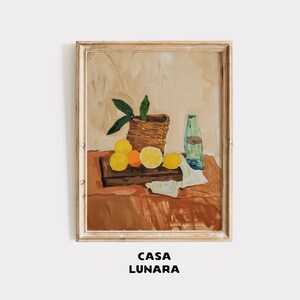 May include: A framed still life painting featuring lemons, oranges, and a bottle. The artwork depicts a woven basket, a wooden cutting board, and a white cloth. The painting has a warm color palette with the text "CASA LUNARA" at the bottom.