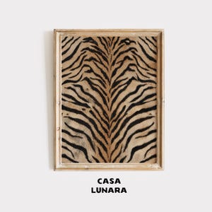Puede incluir: Una pieza de arte mural rectangular con un patrón de rayas de tigre en colores negro y bronceado, encerrada en un marco de madera clara. Debajo de la obra enmarcada, el texto CASA LUNARA está impreso en letras mayúsculas negras y negritas.