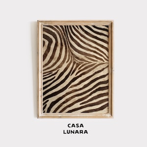 Puede incluir: Una pieza de arte mural rectangular que presenta una impresión de alta resolución de un patrón de rayas de cebra en marrón y crema, encerrada en un marco de madera de tono claro. El texto CASA LUNARA está impreso en letras negras.