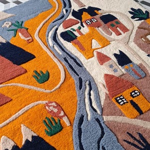 May include: A tufted rug featuring a landscape design with a winding blue river, orange hills, and several small houses in shades of red, yellow, and blue. The scene includes a yellow sun, dark blue mountains, and green plant motifs on a cream background.