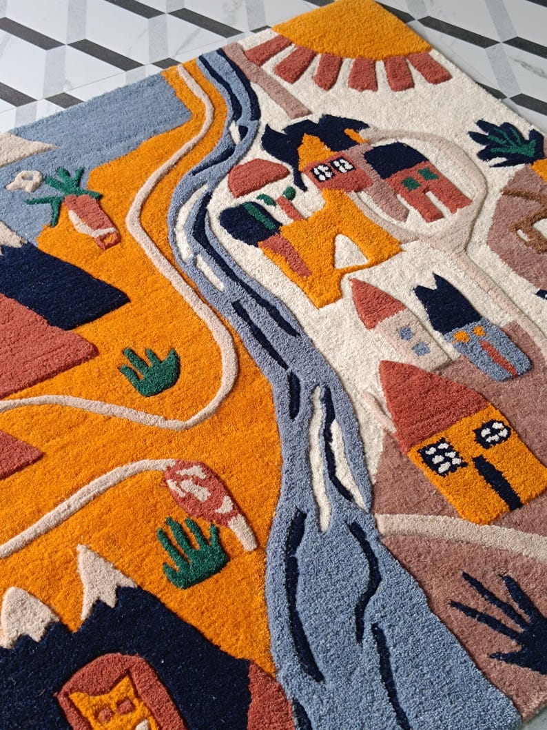May include: A tufted rug featuring a landscape design with a winding blue river, orange hills, and several small houses in shades of red, yellow, and blue. The scene includes a yellow sun, dark blue mountains, and green plant motifs on a cream background.