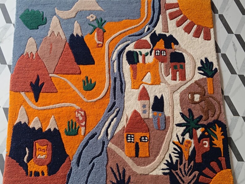 May include: A rectangular tufted rug featuring a landscape design with mountains, a winding blue river, and small houses. The scene includes a lion, palm trees, and a sun in vibrant colors of orange, blue, brown, and cream, creating a textured surface.