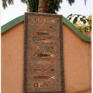 May include: A rectangular rug with a textured brown background featuring ten horizontally aligned fish motifs in various colors including red, blue, orange, and yellow. The rug is framed by a dark border with a repeating white geometric pattern.