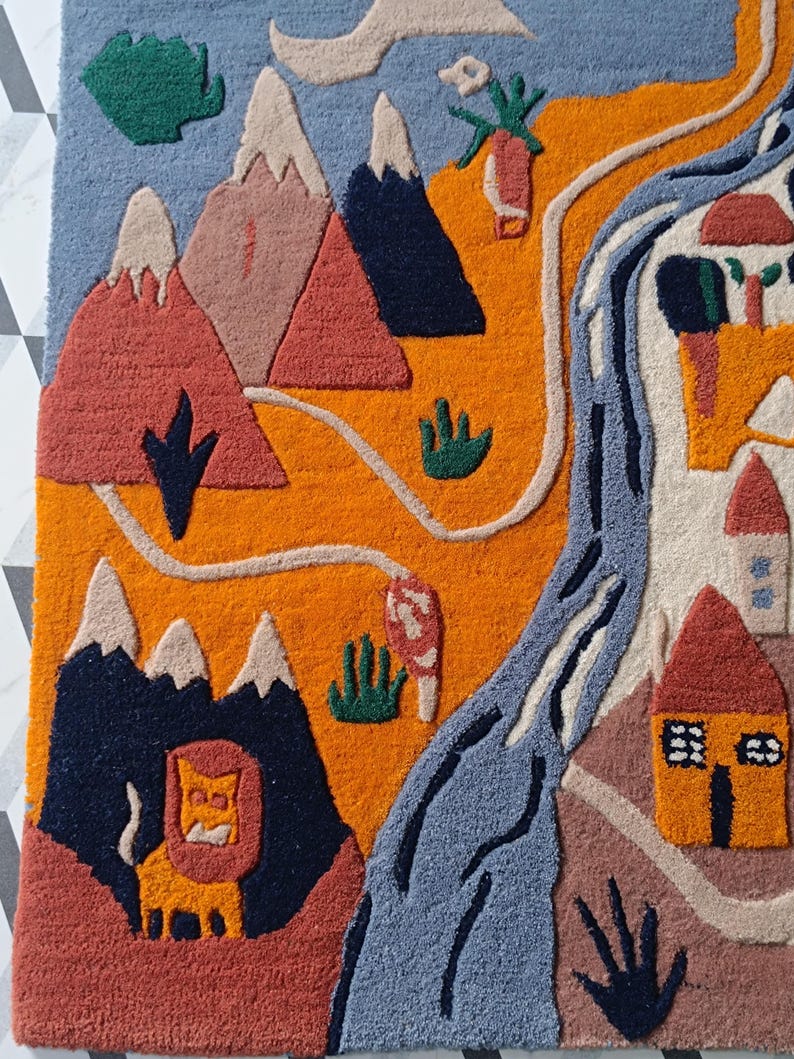 May include: A tufted rug featuring a landscape design with orange fields, blue mountains, a winding blue river, and small houses. The scene includes a yellow lion figure, green shrubbery, and a light blue sky, all rendered in a textured, multi-colored textile.