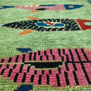 May include: A rectangular runner rug with a light green textured background featuring a repeating pattern of stylized fish in various colors including pink, black, blue, and orange, finished with a dark blue border along the long edges.