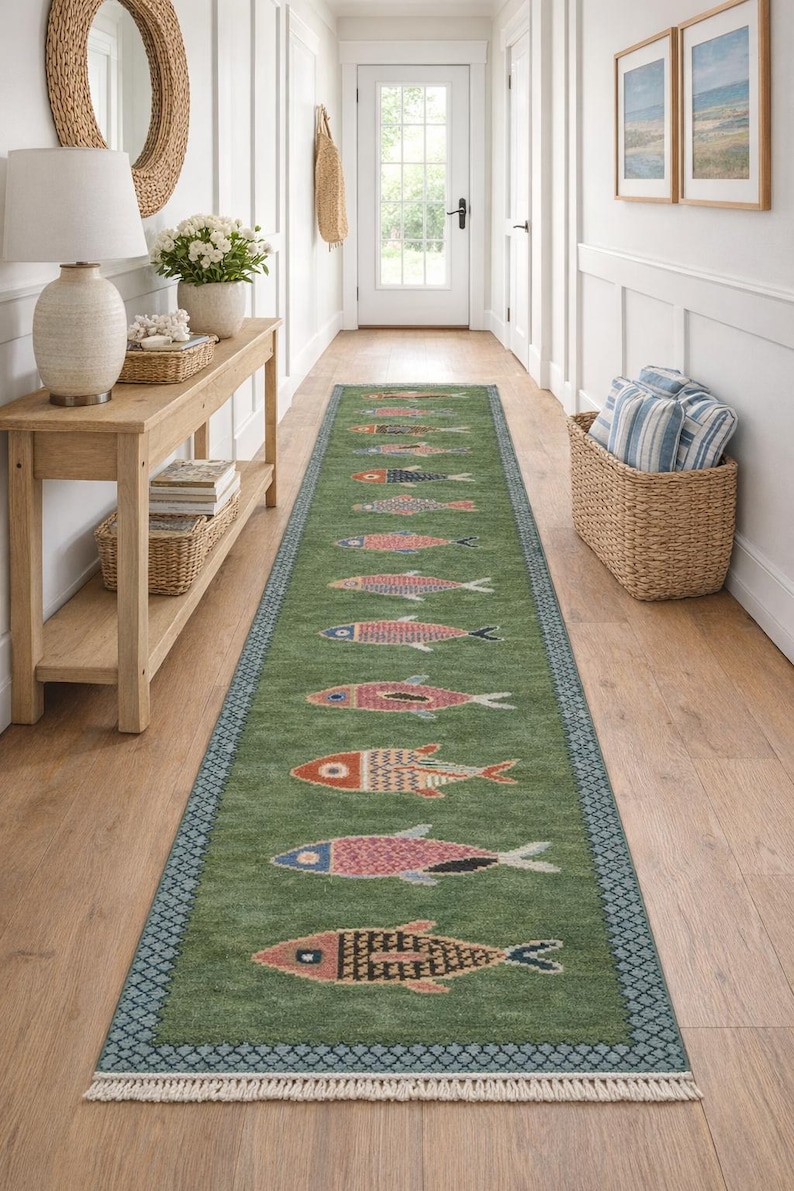 May include: A long, rectangular green runner rug featuring a repeating pattern of stylized fish in various colors including orange, pink, and blue. The rug has a dark blue geometric border and short white fringe along both of the narrow ends.