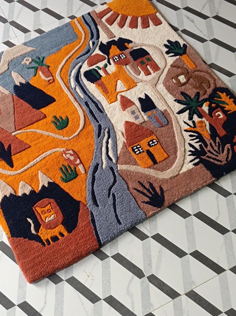 May include: A rectangular tufted rug featuring a vibrant landscape illustration with a bright orange sun, a winding blue river, stylized houses, mountains, and a lion. The design incorporates earthy tones of terracotta, cream, and dark blue.