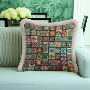 Peut inclure: Un coussin carré orné d'un motif patchwork composé de divers dessins géométriques et floraux colorés dans des tons de rouge, bleu, vert et orange, fini avec une bordure à franges texturée de couleur beige clair sur les quatre côtés.