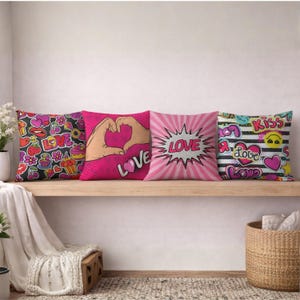 Peut inclure: Quatre coussins décoratifs avec des motifs pop art. L'un a un fond noir avec des autocollants colorés et le mot "LOVE". Un autre présente des mains formant un cœur. Le troisième porte le mot "LOVE" dans une explosion. Le dernier a des rayures et le mot "KISS".