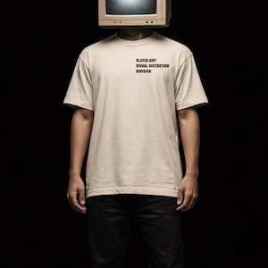 Op de afbeelding: Een persoon draagt een beige t-shirt en een zwarte broek, met een vintage computermonitor in plaats van een hoofd. Op het t-shirt staat de tekst "BLUEBLURY VISUAL DISTORTION DIVISION". De achtergrond is zwart.
