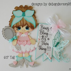 May include: A paper craft doll with brown hair, a pink dress, and silver glitter shoes. The doll is holding a silver mirror with a turquoise bow. The doll is 6.5 inches tall. A banner with the text "Bows & Bling... It's a Diva Thing!!!" is in the background.