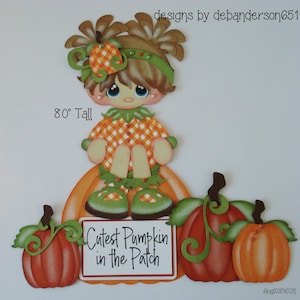 May include: A paper craft cutout of a girl dressed in a plaid shirt and green shoes sitting on a pumpkin. The girl has brown hair and blue eyes. The text "Cutest Pumpkin in the Patch" is on a sign in front of her.