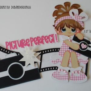May include: A paper cutout of a girl holding a camera, with the words "PICTURE PERFECT!" in pink. The girl is wearing a pink and white checkered dress and shoes. The camera is black and white with a heart design. The cutout is 7.0" tall.