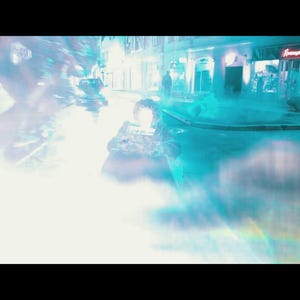 May include: A nighttime street scene with a bright, glowing light source in the foreground. The scene is dominated by a bright, white light with blue and teal hues. Buildings and figures are visible in the background.