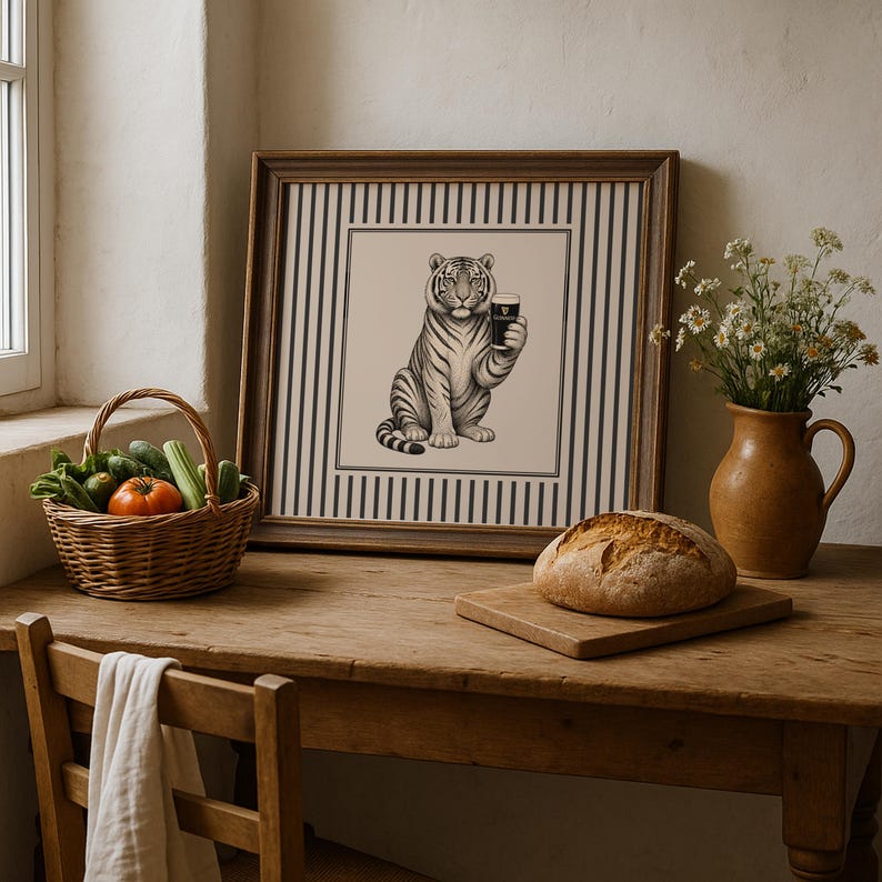 May include: A framed black and white tiger illustration holding a pint of stout. The artwork is set against a striped background. A basket of vegetables, a loaf of bread, and a vase of flowers are on a wooden table.