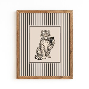 May include: A framed art print depicting a tiger holding a pint of Guinness. The black and white illustration is set against a cream background with a striped border, and is enclosed in a wooden frame. A unique piece of wall art.