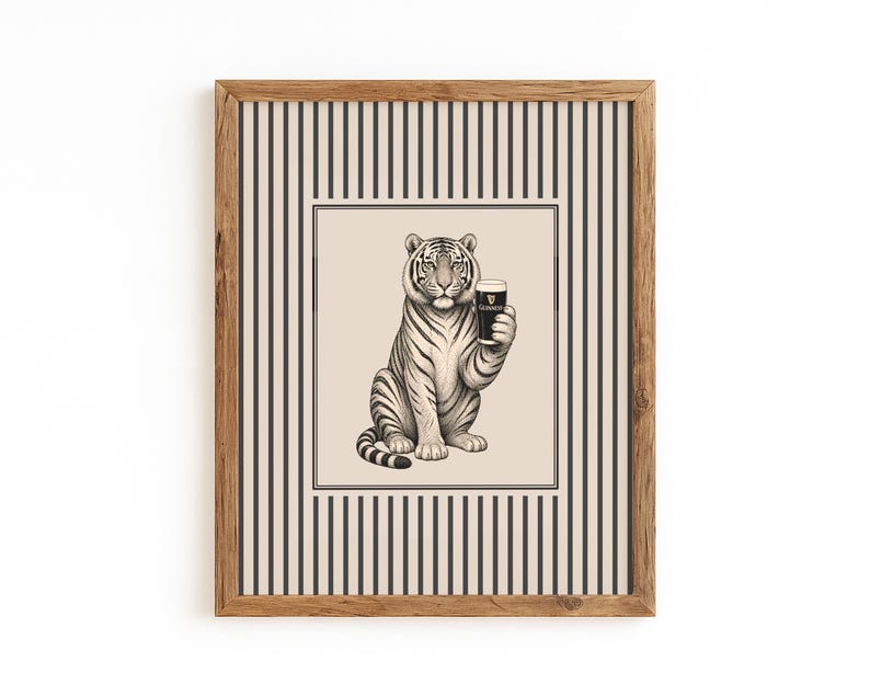 May include: A framed art print depicting a tiger holding a pint of Guinness. The black and white illustration is set against a cream background with a striped border, and is enclosed in a wooden frame. A unique piece of wall art.
