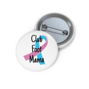 May include: Two white round buttons with a pin back. One button has the text "Club Foot Mama" in black, with a blue and pink ribbon design. The other button is visible in the background.
