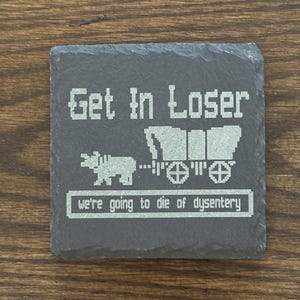 Op de afbeelding: Vierkante leistenen onderzetter met gepixelde tekst en afbeeldingen. De woorden "Get In Loser" staan boven een huifkar en een dier dat hem trekt. Hieronder staat de tekst "we're going to die of dysentery."