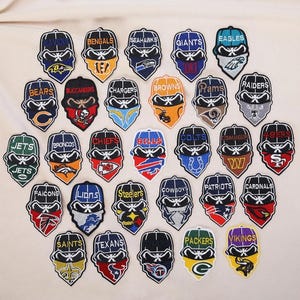 May include: A collection of embroidered patches featuring various NFL team logos. Each patch has a skull-like design with the team's logo and name. The patches are in various colors, including blue, red, yellow, and green.