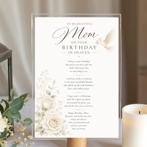 Puede incluir: Un letrero conmemorativo rectangular de acrílico con fondo blanco y un arreglo floral de rosas color crema y follaje a la izquierda. El texto dice: To my beautiful Mom on your birthday in heaven, seguido de un poema y una paloma blanca.