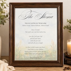 May include: A dark brown wooden frame containing a print of The Shema prayer in English and Hebrew. The text includes the verses from Deuteronomy 6:4-9, set against a soft, light-colored background featuring subtle illustrations of wildflowers.