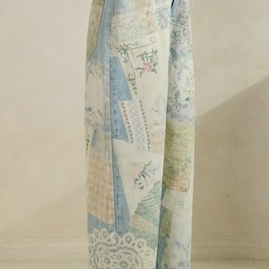 May include: Light blue denim jeans featuring a patchwork design with various printed patterns, including floral motifs, lace-like textures, and geometric shapes in soft pastel colors. The jeans have a high-waisted fit, a button closure, and wide legs.