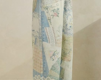 May include: Light blue denim jeans featuring a patchwork design with various printed patterns, including floral motifs, lace-like textures, and geometric shapes in soft pastel colors. The jeans have a high-waisted fit, a button closure, and wide legs.