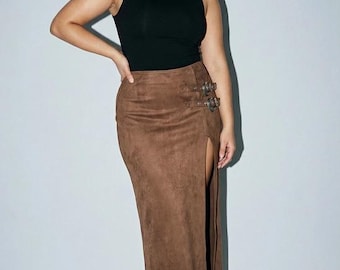May include: A black sleeveless mock neck top paired with a brown suede-textured maxi skirt. The skirt features a high side slit and two decorative silver-toned metal buckles on the upper hip area, complemented by matching brown pointed-toe boots.