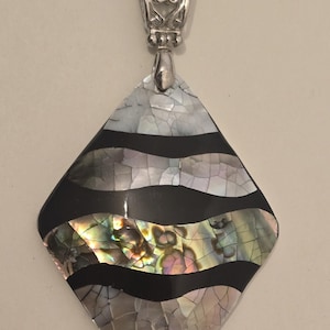 Könnte beinhalten: Silberfarbener Anhänger mit rautenförmigem, schillerndem Abalone-Muscheldesign. Der Anhänger hat abwechselnde Bänder aus Schwarz und der Muschel, mit einer dekorativen silbernen Öse. Die Muschel hat ein rissiges, mosaikartiges Aussehen.