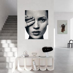 Può includere: Ritratto in bianco e nero di una donna con la mano che copre un occhio. L'immagine è un primo piano, che mostra i lineamenti del viso della donna. L'opera d'arte è esposta su una parete bianca in un interno moderno.