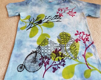 A collage style design on a woman's small t-shirt, dyed, printed, discharged, buildings, birds on branches, leaf motifs, check measurements