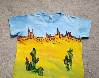 Southwest landscape with cacti, a bird and rock formations, blue sky with oranges & greens, woman's XL screen printed, dyed cotton t-shirt