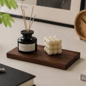 May include: A dark wooden tray holds a black glass diffuser with reeds, a white bubble candle, and a clock. The diffuser has a label that reads "HOME HOME FRAGRANCE FRESH AIR 200ml". The candle is cube-shaped with rounded edges.