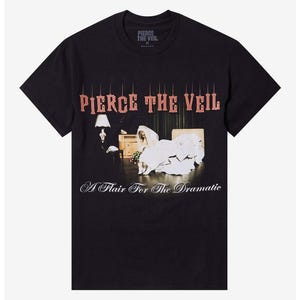 Peut inclure: T-shirt noir avec le nom du groupe "Pierce The Veil" en rouge, dans une police stylisée, au-dessus d'un graphisme de scène. Le graphisme comprend une mariée en robe de mariée et le texte "A Flair For The Dramatic" en cursive.