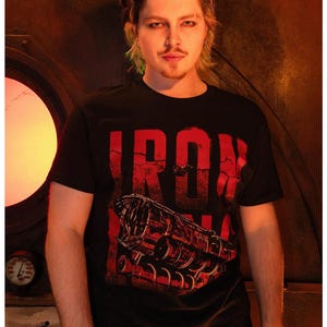 May include: Black t-shirt with the red text "IRON" and a graphic of a train engine. The text and graphic have a distressed, vintage look. The shirt has short sleeves.