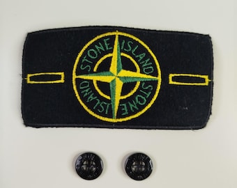 Peut inclure: Un écusson rectangulaire en tissu noir avec un logo boussole brodé en jaune et vert portant l'inscription Stone Island. L'écusson présente deux barres horizontales jaunes et est accompagné de deux petits boutons noirs circulaires à quatre trous.
