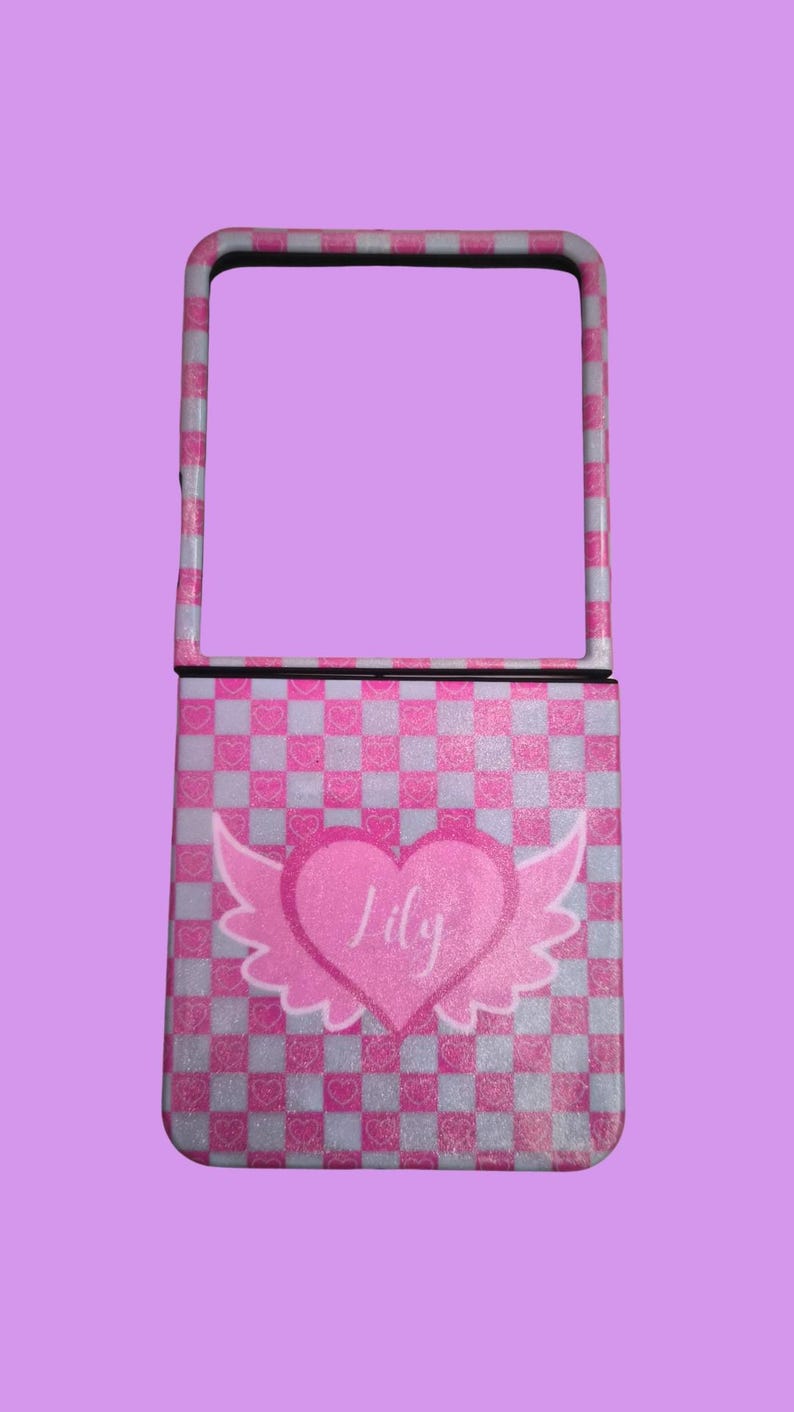 Pu&ograve; includere: Una custodia per telefono pieghevole con un motivo a scacchi rosa e bianco e una finitura glitterata. Il centro mostra un grande cuore rosa con ali d'angelo bianche e il nome Lily scritto in corsivo bianco sulla superficie del cuore.