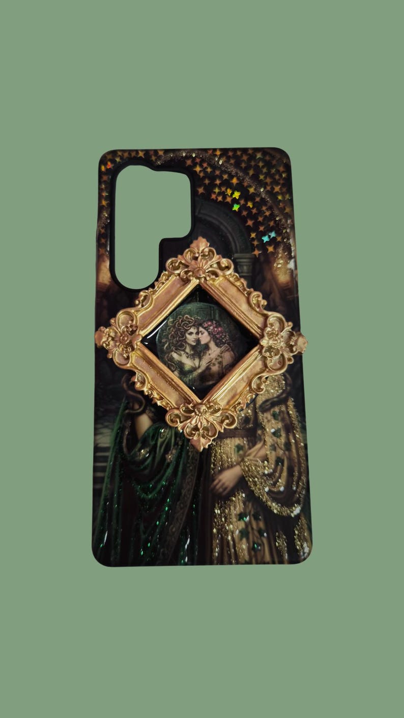 Pu&ograve; includere: Una cover per telefono rettangolare con uno sfondo scuro a motivi stellati e una cornice dorata decorata al centro. All'interno della cornice c'&egrave; un'illustrazione di due figure. La cover mostra anche un'immagine stampata pi&ugrave; grande e parzialmente visibile di due figure con abiti elaborati verdi e dorati.